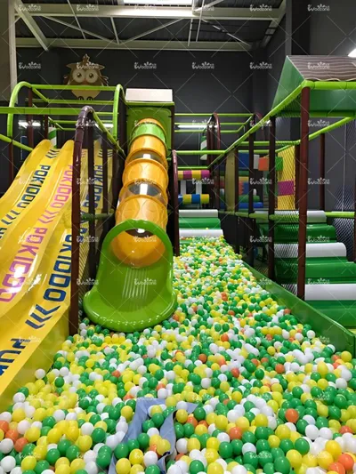 Bright indoor soft play set equipped with yellow multi-lane slide and transparent tube slide, ending in a full colorful ocean ball pit for kids